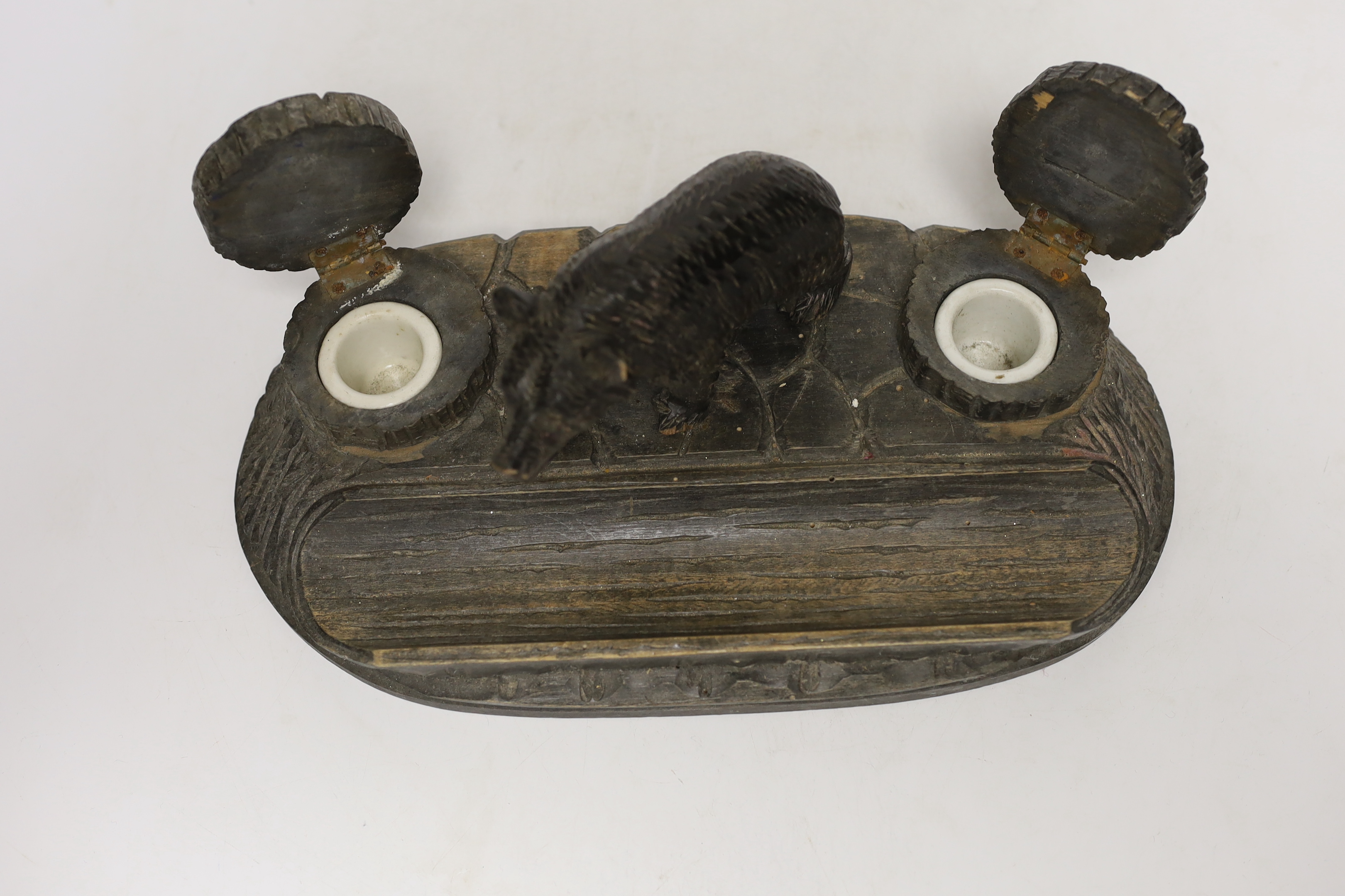 A Black Forest carved wooden inkstand, with ceramic inserts to the inkwells, 31cm wide